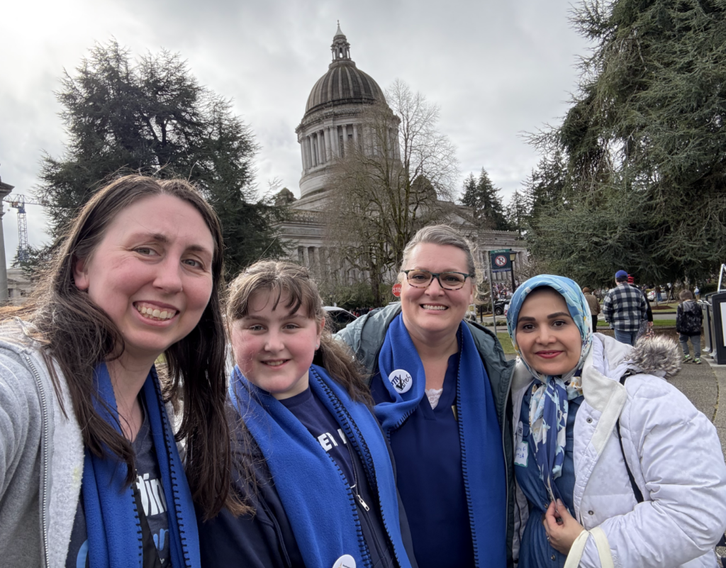 Three adults and one child wearing blue scarves stand in front of the Washington State Capitol building on Feb. 17, 2025, for Washington State PTA's Focus on Advocacy Day.
